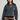 A woman modeling a dark gray crewneck sweatshirt with unique horizontal seam details on the sleeves, paired with blue jeans and a brown plaid shirt tied around her waist, against a light gray studio background.