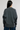 A woman viewed from the back wearing a dark gray knit sweater and blue jeans against a plain light gray studio background.