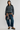 A model stands against a light gray studio background wearing a dark gray crewneck sweatshirt, wide-leg blue jeans with a brown plaid shirt tied around the waist, and brown platform loafers.