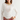 A woman modeling a white ribbed long-sleeve top with lace trim at the neckline and lace panels on the sleeves, paired with pink jeans and layered necklaces, against a plain light gray studio background.