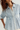 A close-up of a woman wearing a light blue and white vertically striped button-down shirt with a chest pocket and a peplum waist detail.