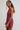 A woman modeling a sleeveless, high-neck mini dress with a burgundy and gold plaid pattern, photographed against a neutral light gray studio background.