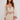 Woman wearing a beige dress with red floral embroidery on a plain background