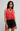Woman wearing a coral top and black lace shorts on a plain background
