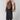 A model wearing a black halter midi dress with a large floral embroidered bodice panel, styled with a light beige faux fur jacket and black leather boots against a light gray studio background.