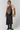 A model wearing a black halter midi dress with a large floral embroidered bodice panel, styled with a light beige faux fur jacket and black leather boots against a light gray studio background.