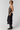 A woman models a black halter-neck midi dress with a floral embroidered bodice panel, paired with black leather boots, against a plain light gray studio background.