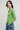 Woman wearing a green sweater and blue jeans against a plain background