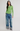 A woman modeling a light green ribbed long-sleeve top, blue wide-leg jeans with rolled cuffs, and black and white sneakers against a plain light gray studio background.