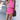 Woman in a pink outfit with a black bag standing against a white wall.