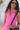Woman wearing a pink sleeveless top with a black strap over her shoulder, outdoors.