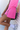 Person wearing a pink skirt with a small logo, standing against a light-colored wall.