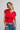 Woman wearing a red top and blue jeans against a plain background