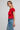 Woman wearing a red top and blue jeans on a plain background