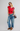 Woman wearing a red top and blue jeans with a colorful bag on a white background