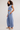 A woman modeling a light blue two-piece loungewear set consisting of a sleeveless ruched crop top and matching wide-leg pants, paired with beige slide sandals against a plain light gray studio background.