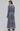 A woman wearing a long-sleeved, tiered midi dress in a dusty slate blue-gray color, shown from the back against a plain light gray studio background.