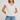 Woman wearing a white blouse with ruffled sleeves and denim shorts on a plain background