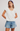 Woman wearing a white blouse with ruffled sleeves and denim shorts on a plain background