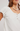 Woman wearing a white blouse with ruffled sleeves and a necklace on a plain background