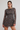 A woman modeling a long-sleeve brown mini dress with a blue and pink fish pattern, set against a plain light gray studio background.