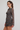 A woman modeling a sheer brown long-sleeve mini dress with a colorful cloud pattern, photographed against a plain light gray studio background.