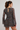 A woman shown from the back wearing a sheer brown long-sleeve mini dress with a small-scale multicolor floral print and a tie waist.