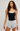 A woman modeling a black camisole tank top with a white trim and light gray drawstring shorts against a light gray studio background.
