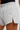 Close-up of a person wearing light heather gray sweat shorts with a drawstring waist, side slit, and a small embroidered leaf logo on the front.
