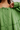 Close-up of a person wearing a loose sage green blouse with a tie neckline, front buttons, and embroidered trim details.