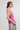Woman wearing a pink knitted tank top and striped pants on a white background