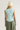 A woman shown from the back wearing a light mint sleeveless athletic top, olive green pants, and a cream beanie against a plain light gray studio background.