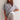 A woman wearing a loose, oversized heather gray t-shirt layered over a white undershirt and light beige jeans, posing against a plain off-white wall.