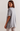 A woman wearing an oversized light gray heather t-shirt with a layered under-sleeve design, shown from a side-back angle against a plain off-white background.