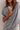 A woman wearing a heather gray oversized draped tunic top over a white crewneck t-shirt, shown in a close-up shot against a neutral light beige wall.