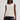 A woman modeling a sleeveless cream-colored knit vest with black faux-leather shorts against a plain light gray studio background.