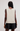 A model shown from the back wearing a cream-colored, sleeveless, textured knit vest and black shorts against a plain light gray background.