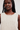 A close-up of a model wearing a cream-colored, sleeveless chunky knit top against a plain light background.