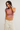 Woman wearing a pink crop top and beige pants on a plain background