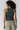 A woman shown from the back wearing a dark teal ribbed tank top and light olive pants against a light gray studio background.
