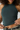 A close-up of a woman wearing a dark teal green ribbed knit halter crop top, lifting the hem with her hands to show the fit.