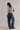 A model shown from behind wearing a beige cropped knit sweater and wide-leg blue denim jeans, paired with brown shoes, against a plain light gray studio background.