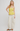 Woman wearing a yellow checkered top and white pants on a plain background