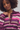 A close-up of a woman wearing a fuzzy knit cardigan with horizontal stripes in purple, pink, beige, and white, featuring a buttoned collar neckline.