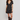 A woman modeling a short-sleeve black wrap-style mini dress with a beige and white floral print, paired with dark brown knee-high leather boots, against a plain light gray studio background.