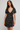 A woman modeling a short-sleeve wrap-style dress with a ruffled V-neckline and a beige floral print on a black background, photographed against a plain light gray studio backdrop.