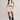 Woman wearing a white crop top, white skirt, and black boots on a plain background