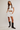 Woman wearing a white crop top, white skirt, and black boots on a plain background