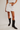 Person wearing a white skirt and black cowboy boots on a plain background