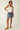 Woman wearing a white tank top and denim skirt on a plain background